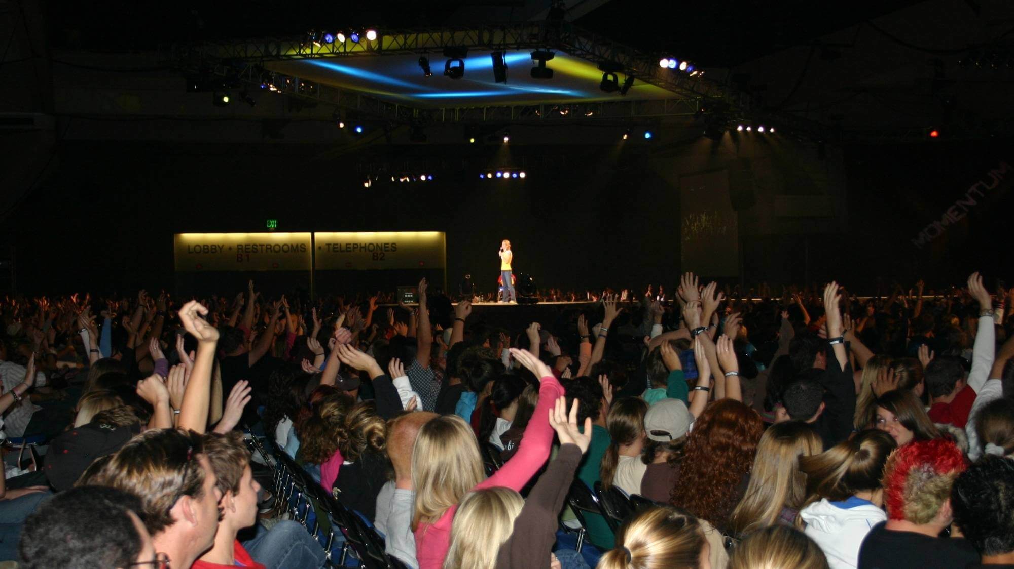 Woman speaking on big stage with audience raising their hands